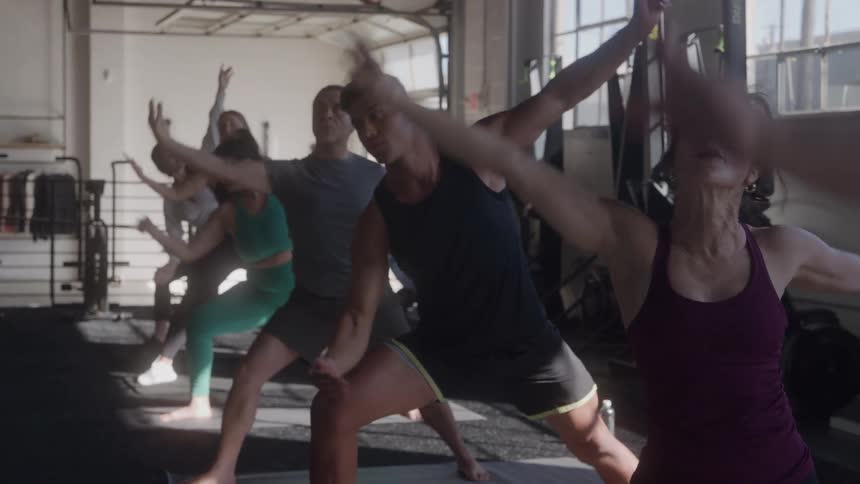 A group of people practice yoga stretches together in a gym