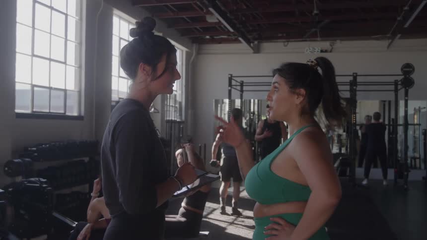 A woman is listening and taking notes from another woman in the gym
