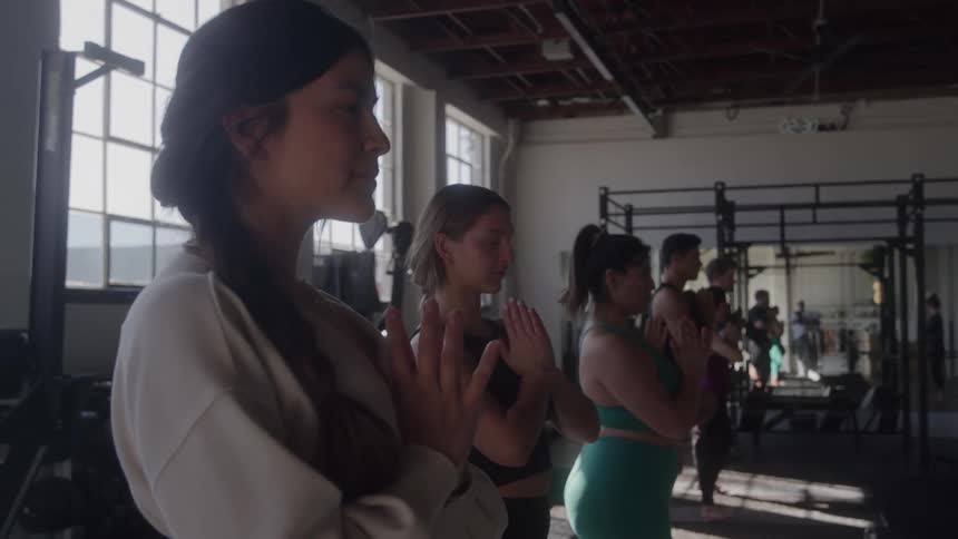A group practices yoga in a gym with hands in prayer pose