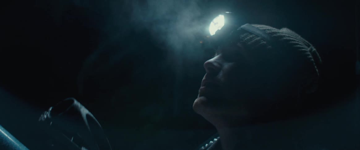 The video shows a person using a telescope at night a closeup shot focuses on their face which is illuminated by a headlamp as they look up from the telescope with a sense of wonder