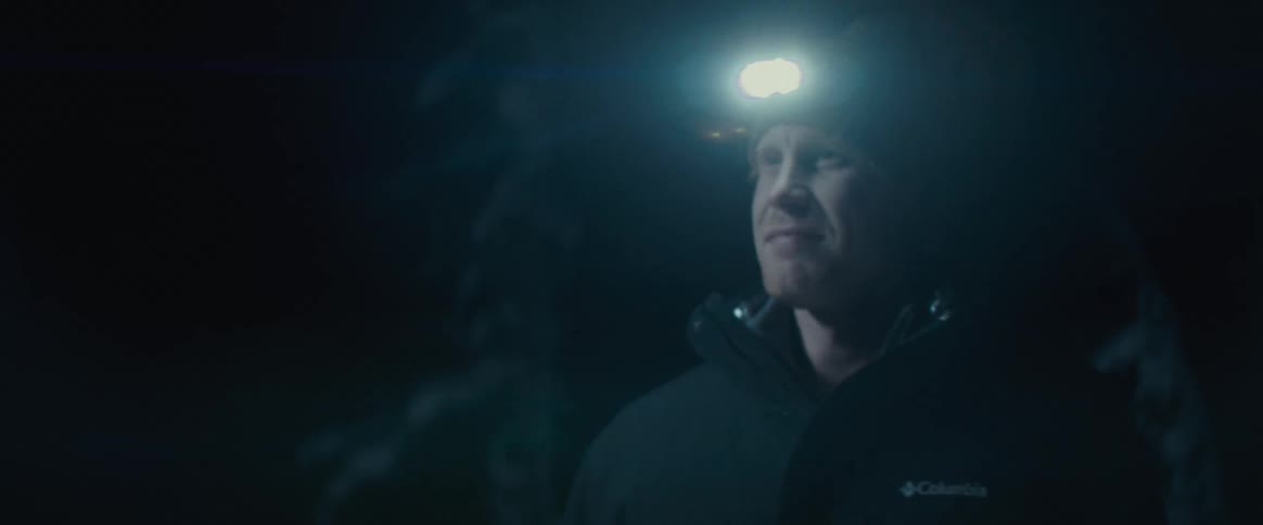Middleaged man wearing a head torch walking through a dark forest with a smile on his face