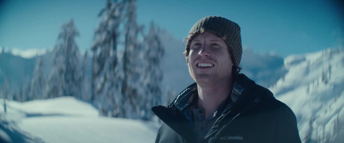 A man smiles overlooking snowy mountains in winter under a bright sky