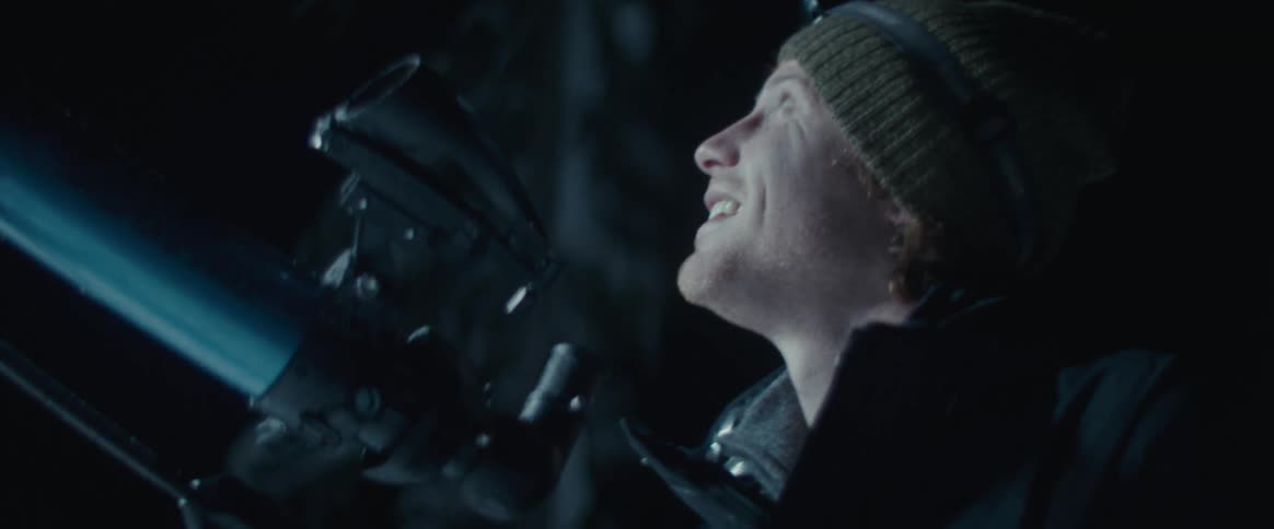 A man observes the starry night sky through a telescope
