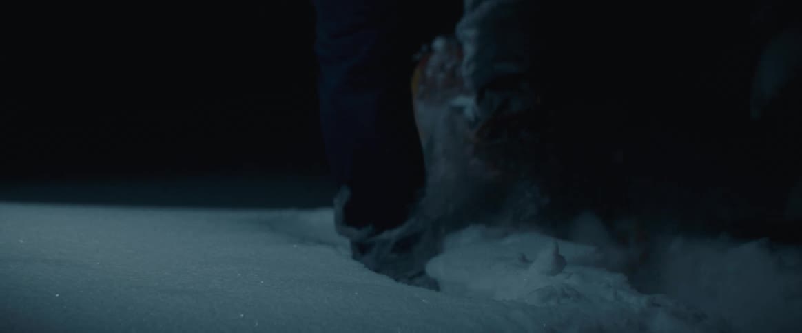 The video shows a person walking in the snow at night a closeup shot focuses on their feet as they walk revealing that they are wearing snowshoes to navigate the deep snow
