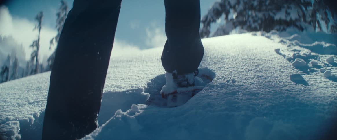 A close view shows a person wearing snowshoes as they walk through deep fresh snow on a sunny winter day
