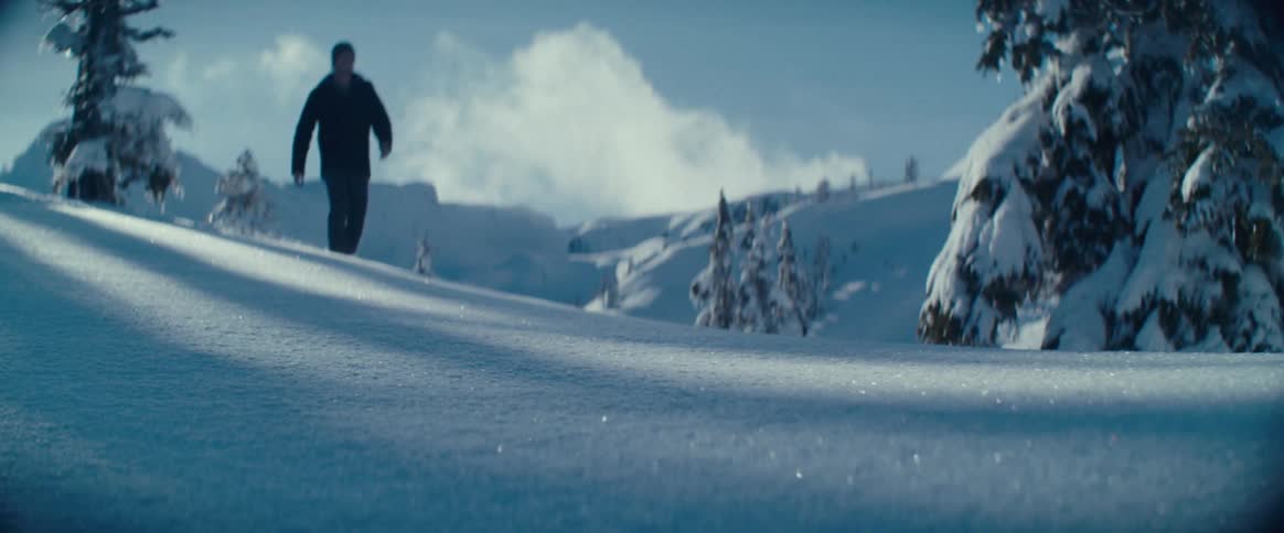 The man is wading through the deep snow wearing snow shoes