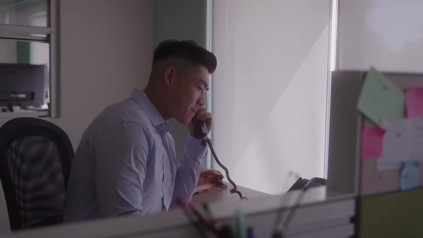 Young man sitting behind a desk in his office at midday making a call on the office telephone
