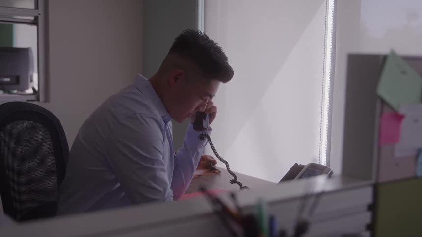 A man talks on a landline phone at his office desk