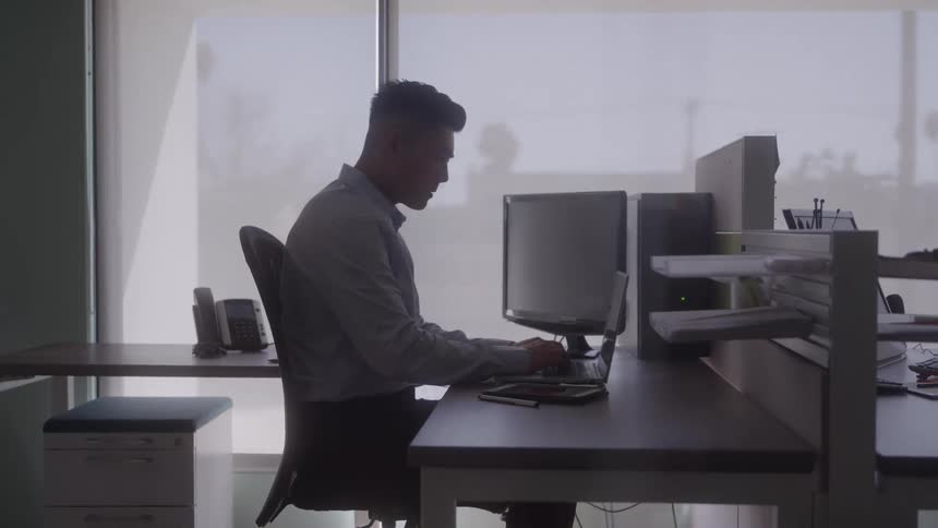 A man works alone at his desk in a modern office cubicle
