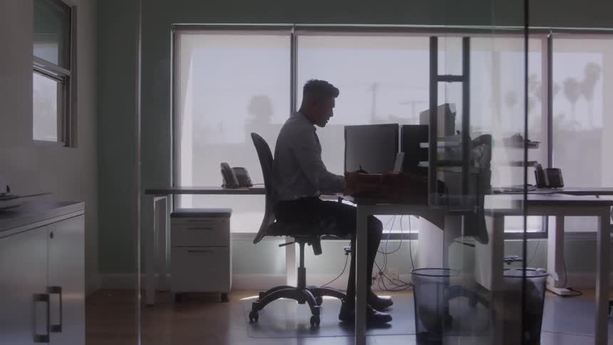 A young man sits at a desk in an office and its working writing something
