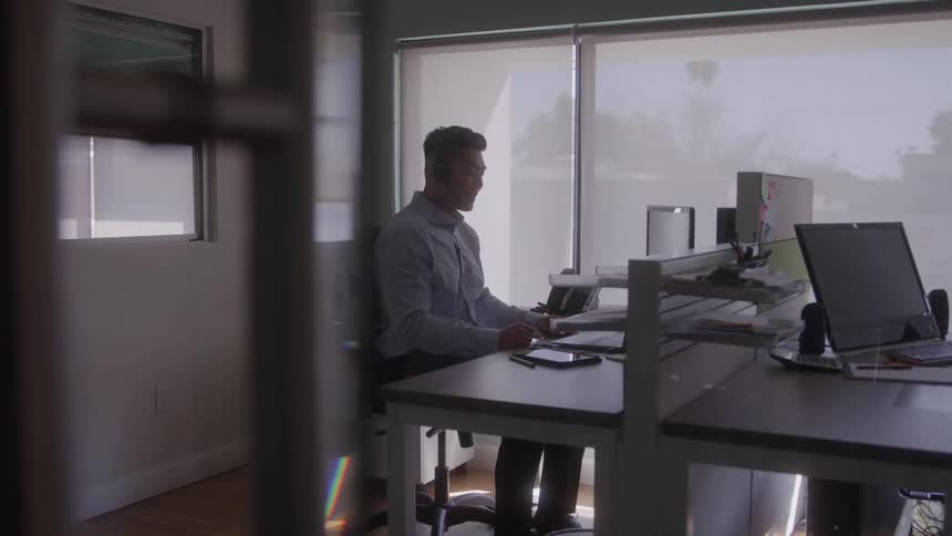 Man wearing headphones works at a computer in a bright office