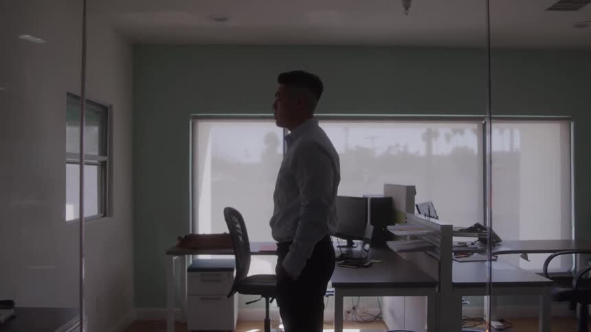 Asian young man wearing a tucked longsleeve shirt standing in his office deep in thought