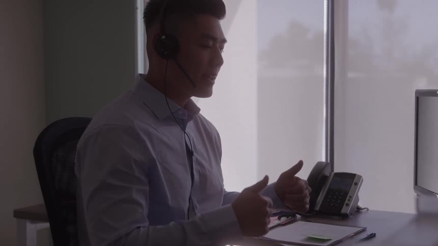 A man with a headset gestures while working at his office desk