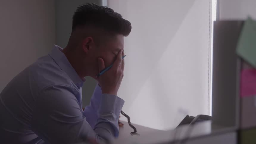 The video shows a man sitting at his desk holding a telephone receiver and looking distressed he brings his hand to his face in a gesture of frustration or sadness suggesting he has received some bad news
