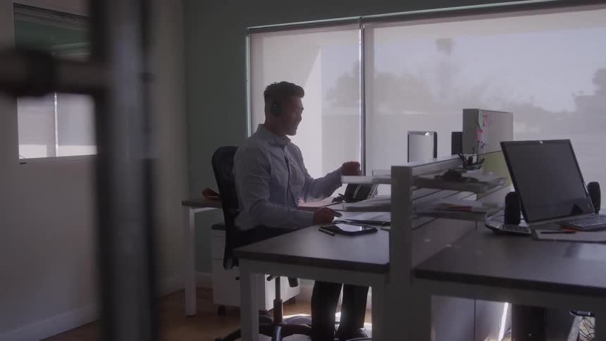 A male customer service agent talks to a customer at a call center desk