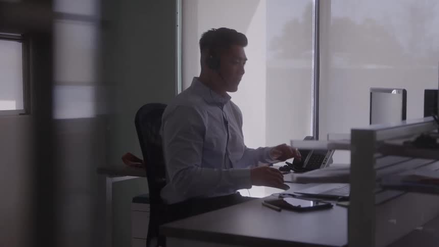 A male customer service agent works at his desk in a call center