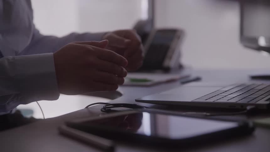 A person gestures while working on a laptop at a desk