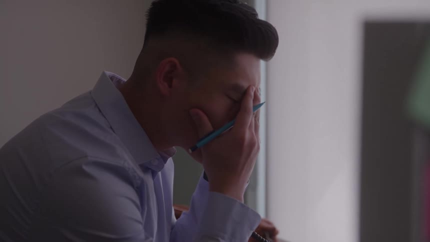 Close up of a young asian man taking a telephone call while sitting at a table in an office during daytime