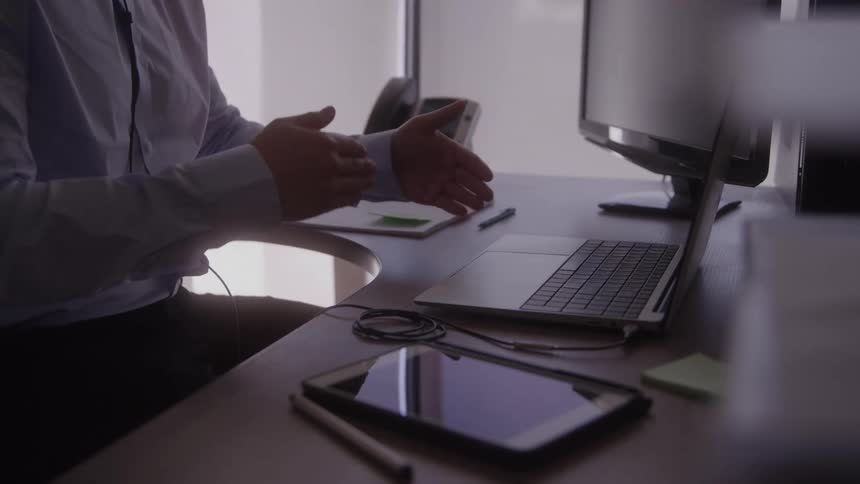 A man gestures while speaking at his desk in an office
