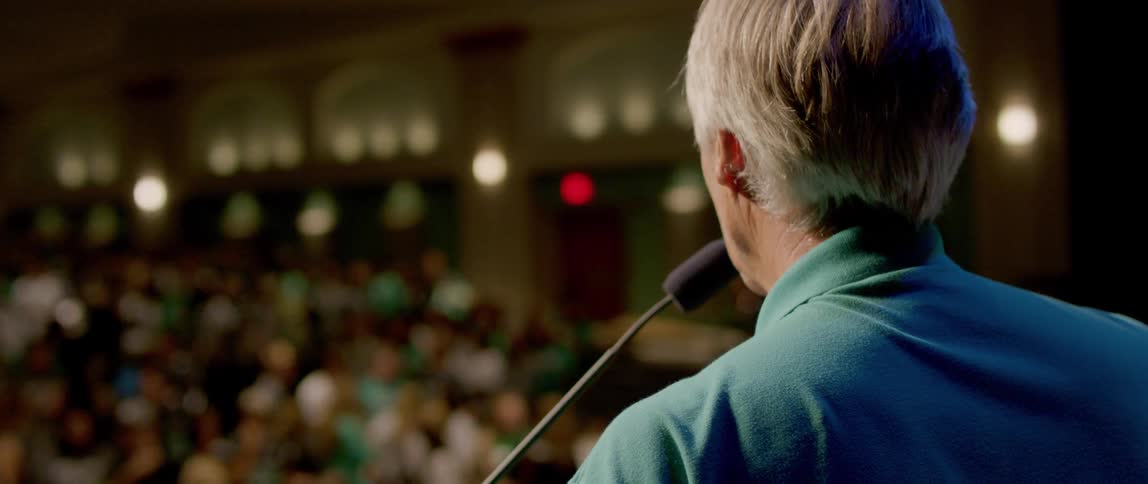 Man speaking into a microphone from a pulpit to a crowd of people