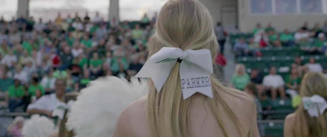 Cheerleader with a white bow in her hair dancing in front of the crowd