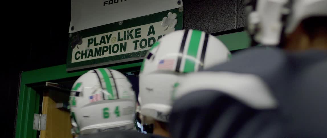 Football players tap a sign as they enter the locker room