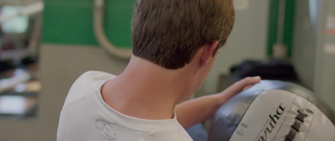 The video shows a person using a medicine ball for an exercise they are seated with their back to the camera repeatedly lifting the ball from the floor to just above their head in a controlled motion