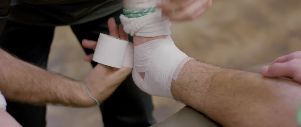 Pair of hands of a person bandaging another persons ankle