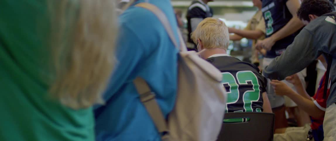 The video shows a group of american football players in their locker room two of the players are sitting at a table with their backs to the camera wearing black and green jerseys
