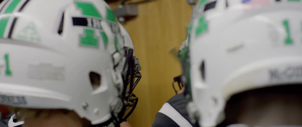 A group of male football players in white helmets adjust helmets with green markings