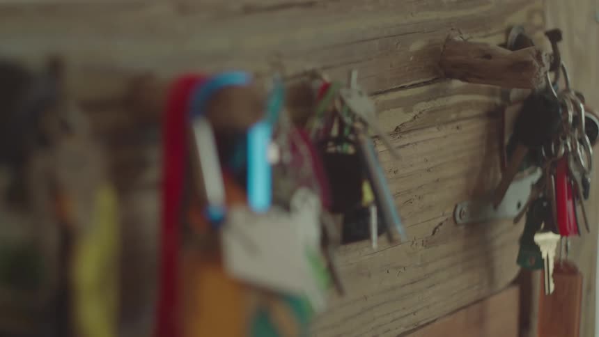 A medium closeup shot of a wallmounted key holder which has several sets of keys hanging from hooks the key holder itself is made of rustic lightcolored wood