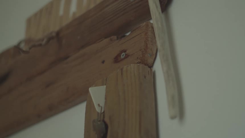 A key is hanging from a hook on a wooden key holder mounted on a wall the wood is rustic and has visible grain and imperfections
