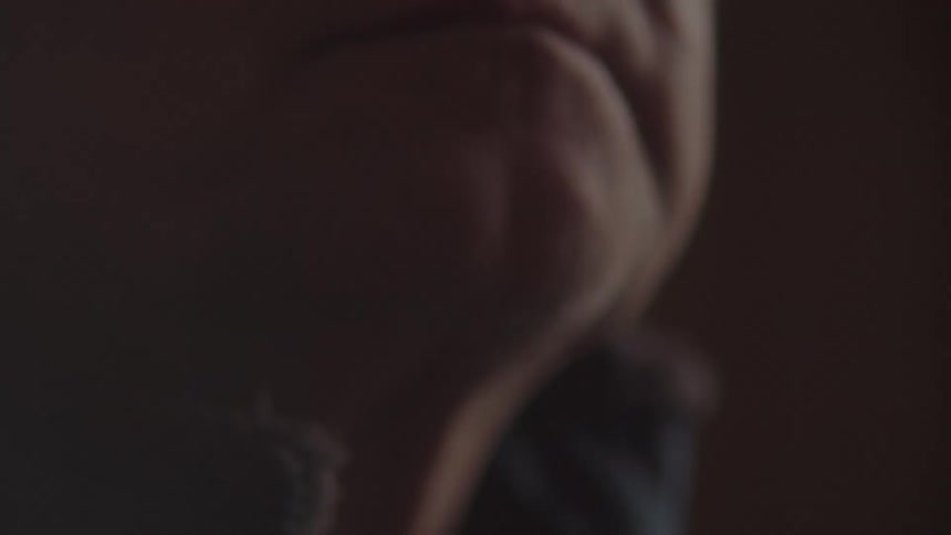 In a dimly lit setting a persons wrist with a watch is shown followed by a close up of their mouth
