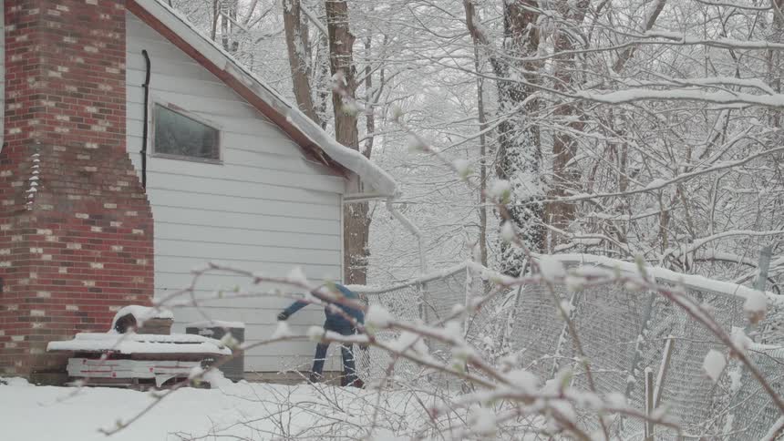 The man is wiping snow off the side of his house