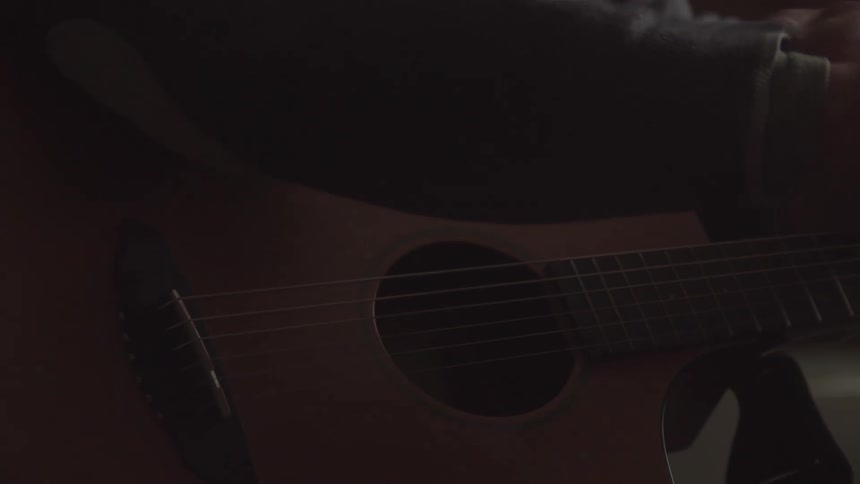 A person wearing a gray hoodie is playing a song on an acoustic guitar the shot is a closeup of the guitar and the persons right hand strumming the strings