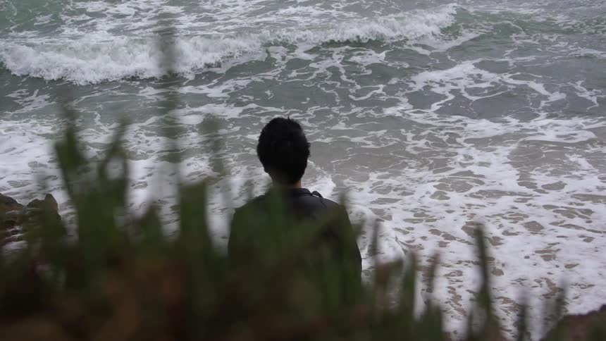 Man watches the waves crash against the rocks