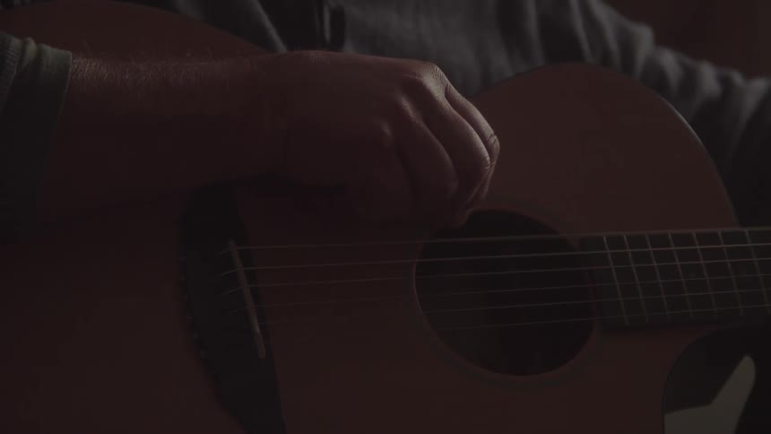 Hand of a male musician tuning an acoustic guitar indoors during day time