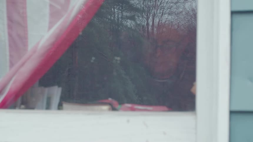 An elderly mans reflection is faintly visible in the window of a house