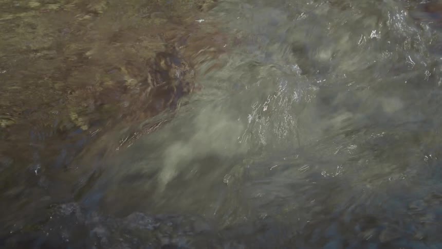 The water is flowing quickly over some rocks the water is clear enough to see the rocks beneath the surface