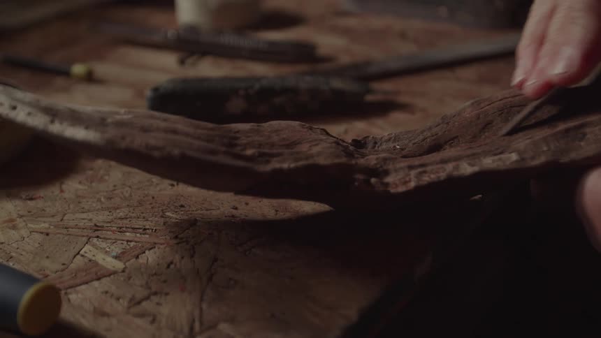 The man is using a chisel on a piece of wood