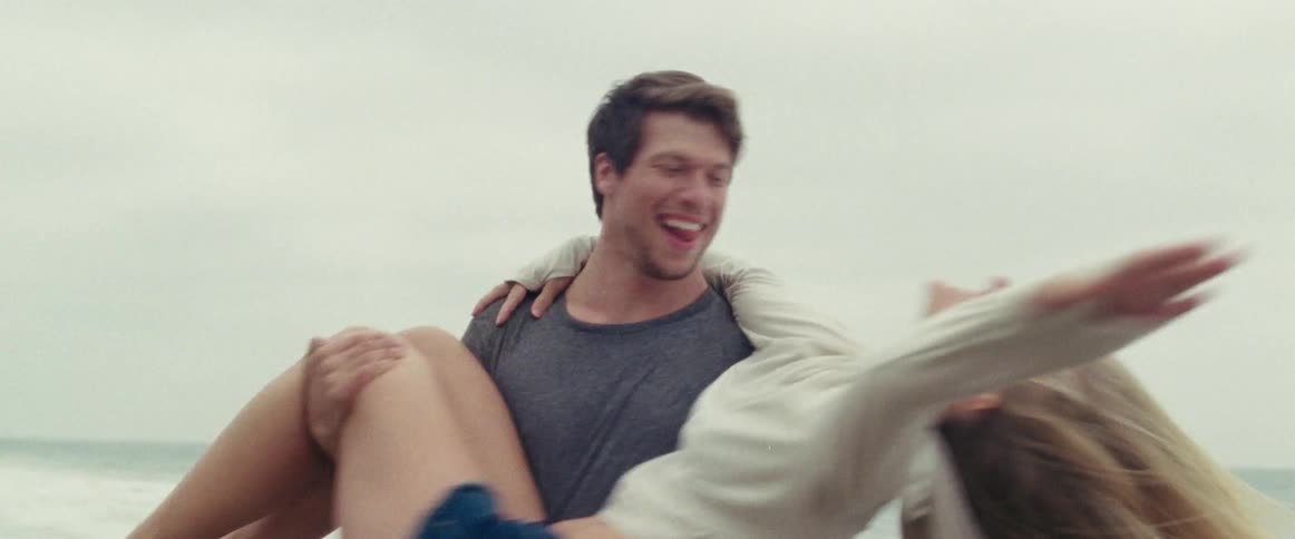 A man and a woman at the beach and he is spinning her around as he holds her