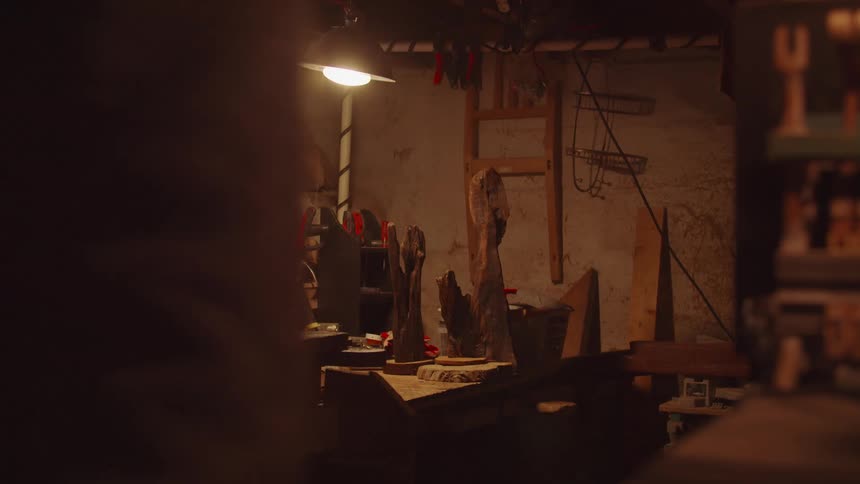 A person walks into a dimly lit wooden workshop with various tools and wooden projects visible on the walls and workbenches