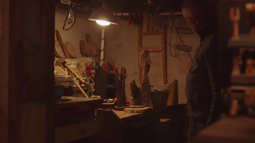 Man observing wood carvings in a shed