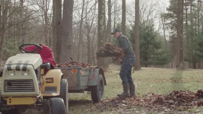 The man is shoveling leaves into the trailer
