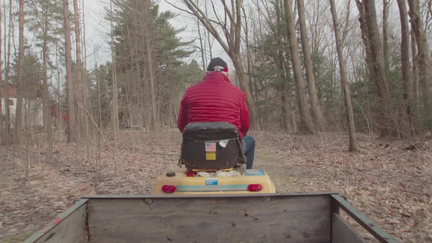 Man in a red jacket drives a tractor on a dirt path in the forest