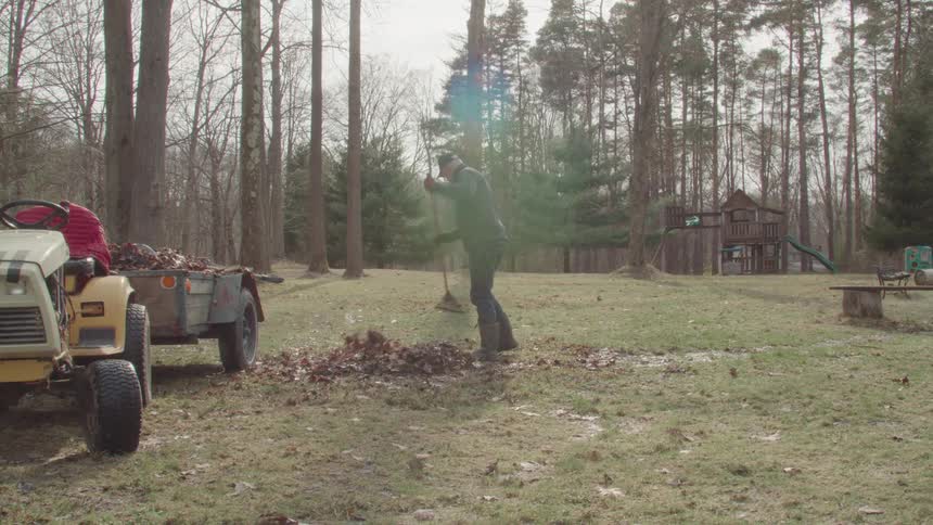 The man is raking leaves on the large field