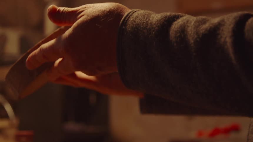 A person holds a piece of wood and uses a square piece of paper to rub the surface