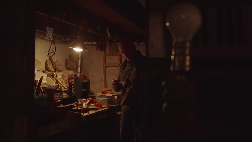 Man applying paint to a piece of wood on his workbench inside his garage workshop