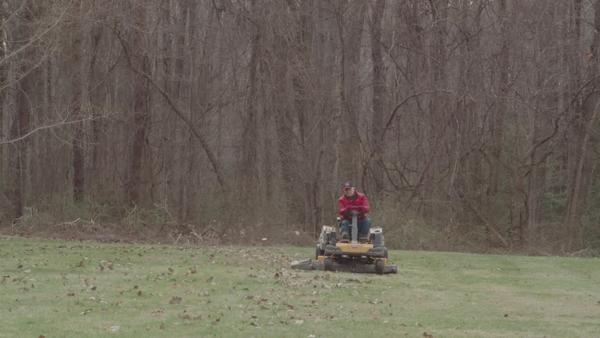 The man rides the lawnmower over the leaves