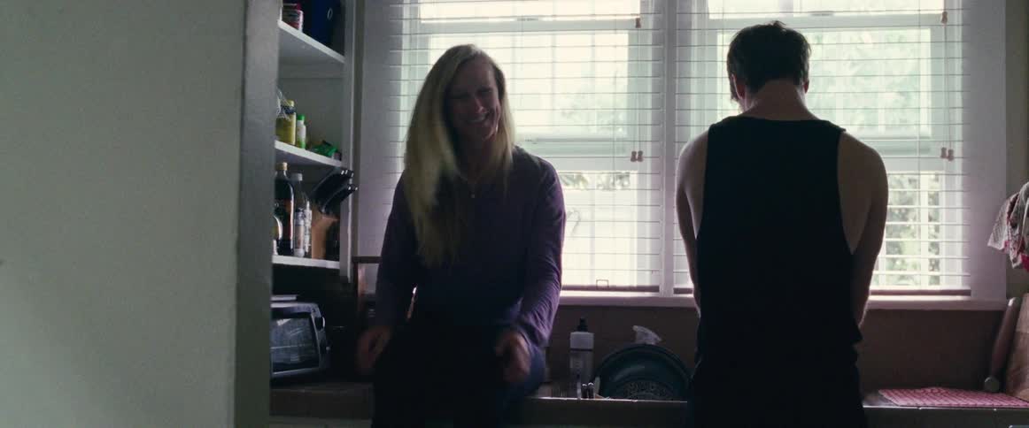 Smiling woman laughs and sits on a kitchen sink while man washes dishes